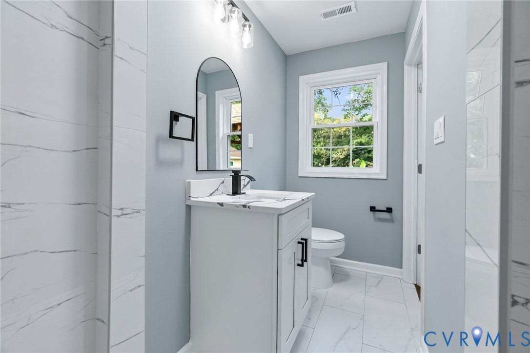 Bathroom featuring a white vanity with integrated sink, arched mirror, black faucet, and tiled shower surround