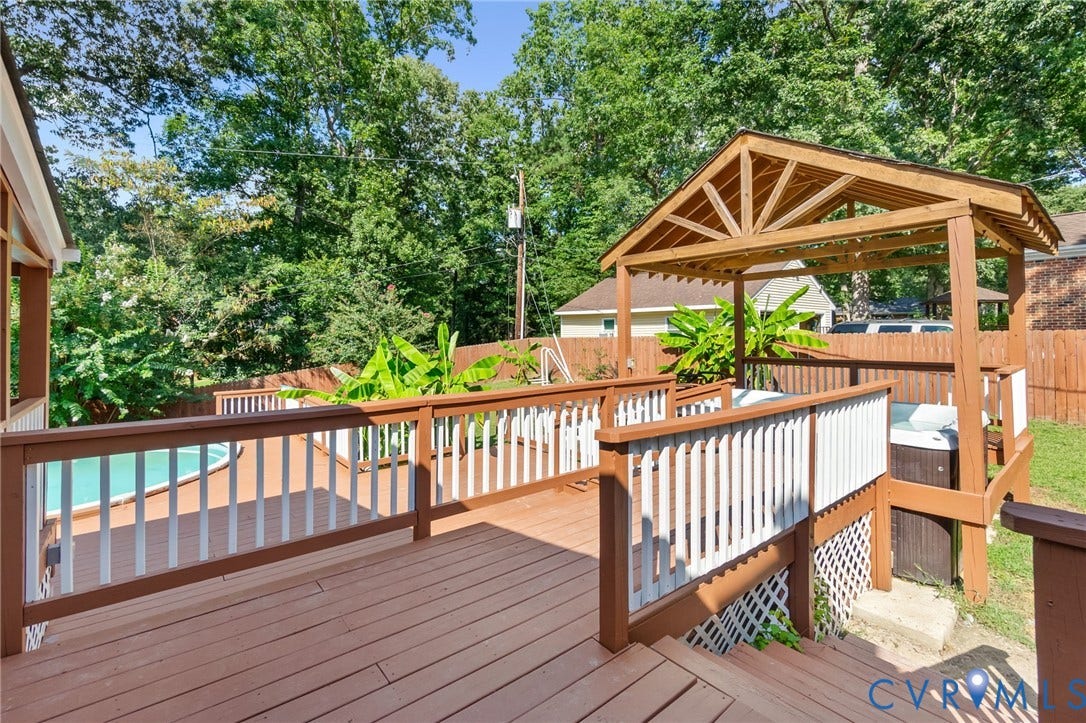 Expansive wood deck with white railings, a built-in spa, and a wooden gazebo
