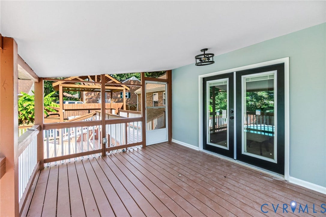 Covered outdoor deck with wood-finish flooring, white railing, and a black double-door entry