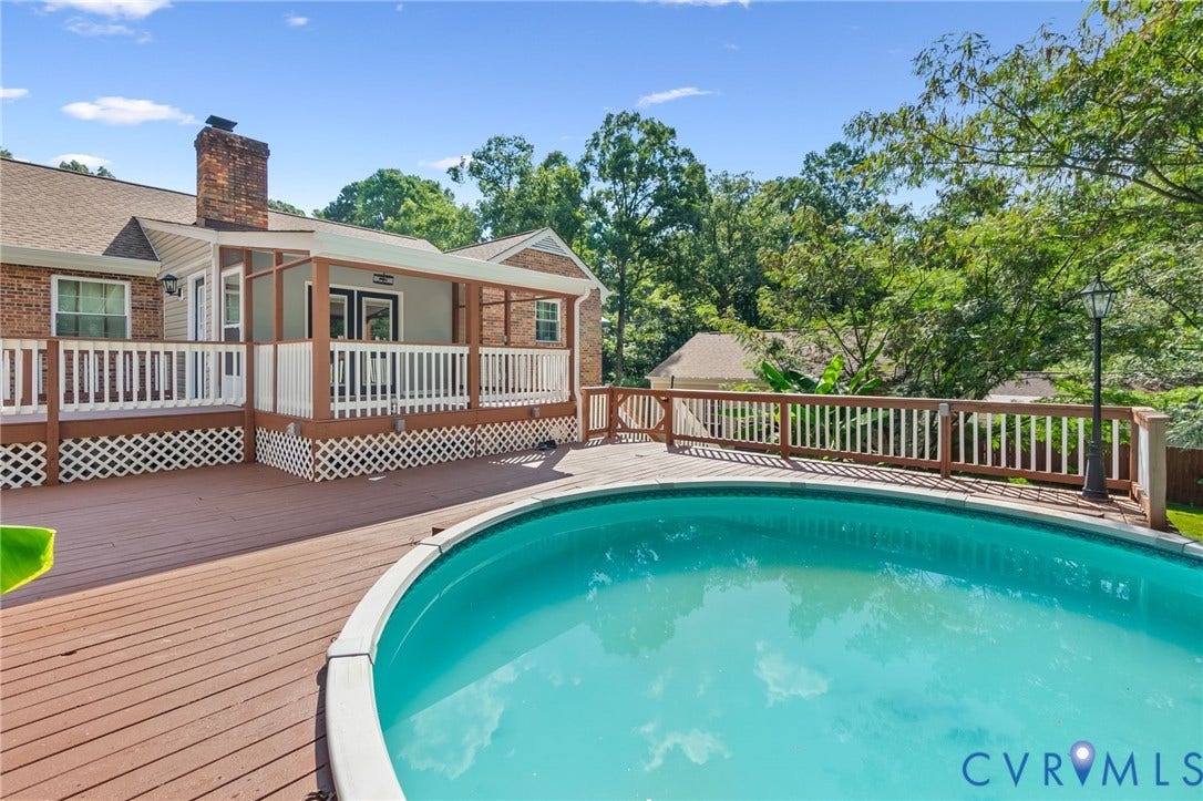 Brick Colonial residence featuring a wraparound deck with white railings overlooking an in-ground swimming pool with turquoise finish