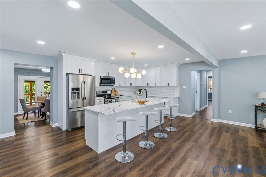Open-concept kitchen with wood-finish flooring, white cabinetry, stainless steel appliances, and a central island with a quartz countertop