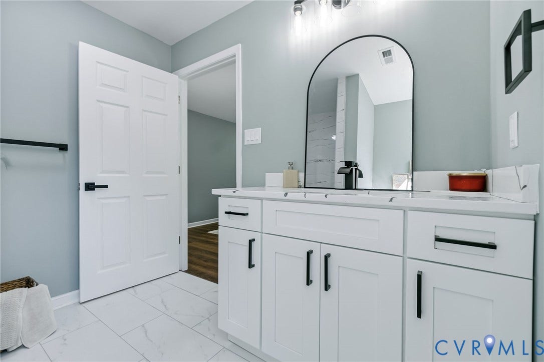 White shaker-style vanity with matte black hardware, white countertop, integrated sink, and an arched mirror