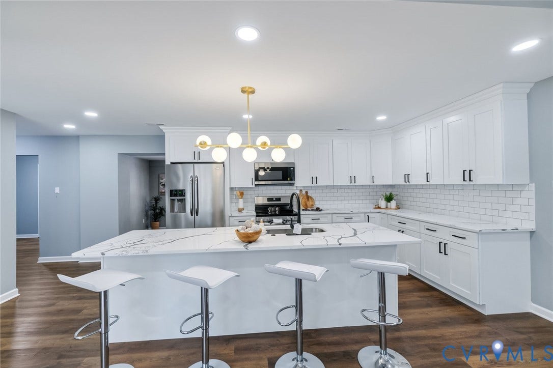 Kitchen featuring white shaker cabinetry, stainless steel appliances, a large island with a waterfall edge countertop, and wood-finish flooring