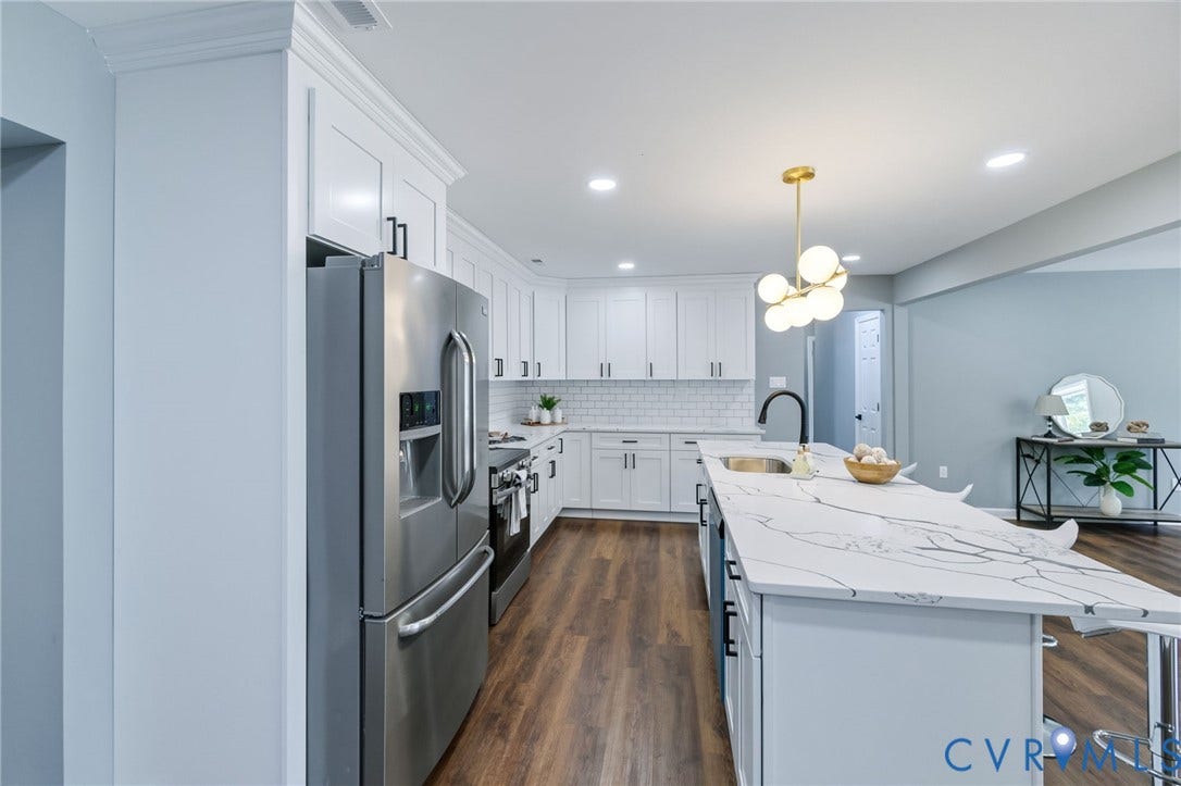 Kitchen featuring white cabinetry, stainless steel appliances, wood-finish flooring, a white subway tile backsplash, and an expansive island with a waterfall countertop