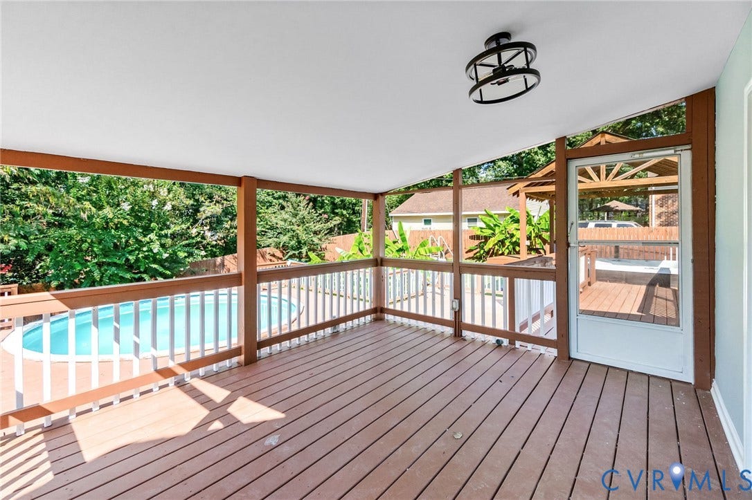 Covered deck with a ceiling-mounted light fixture, wood-finish decking, and white railings overlooking a swimming pool