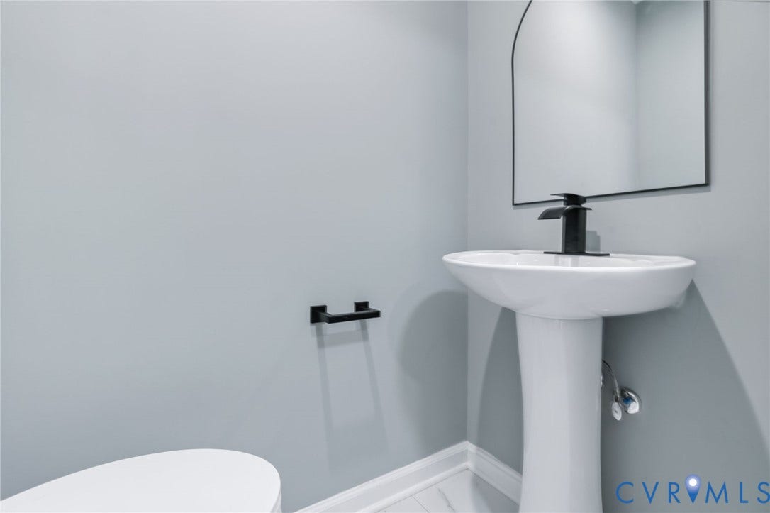Pedestal sink with a matte black faucet, wall-mounted mirror, and light gray walls