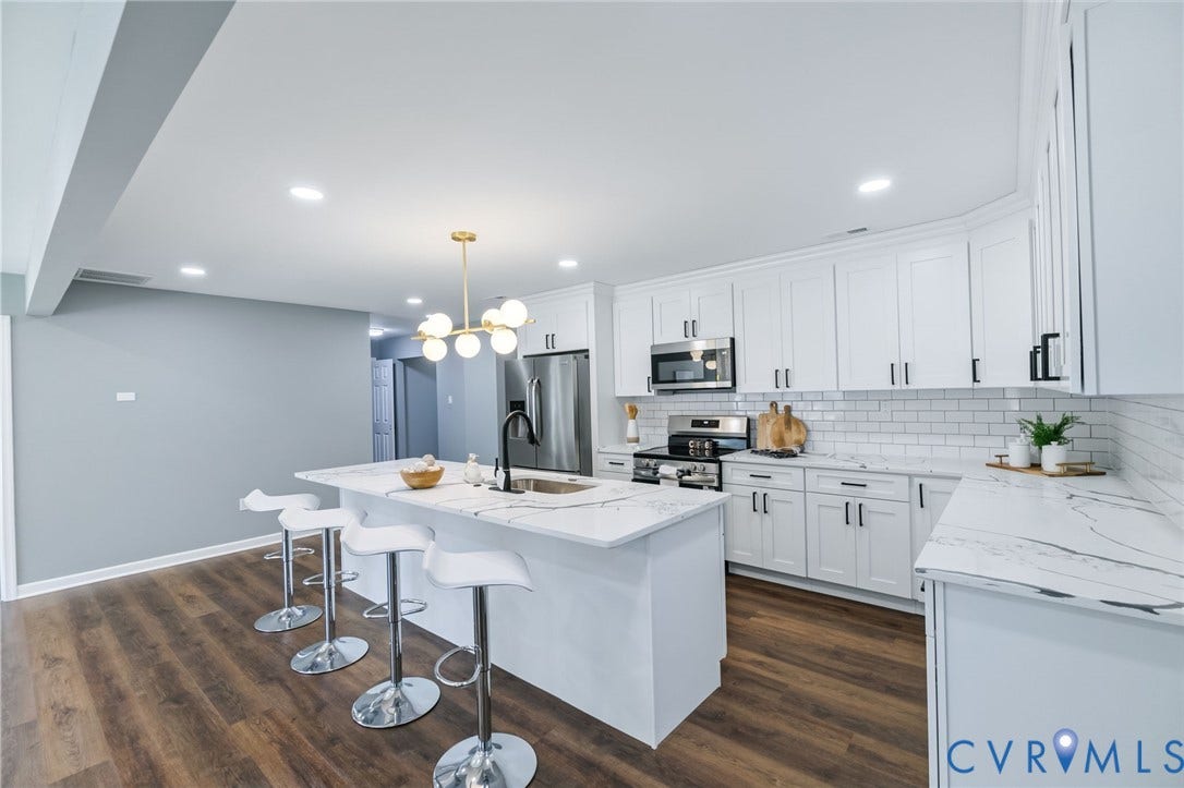Kitchen featuring an island with a sink, white cabinetry, integrated stainless steel appliances, a subway tile backsplash, and wood-finish flooring