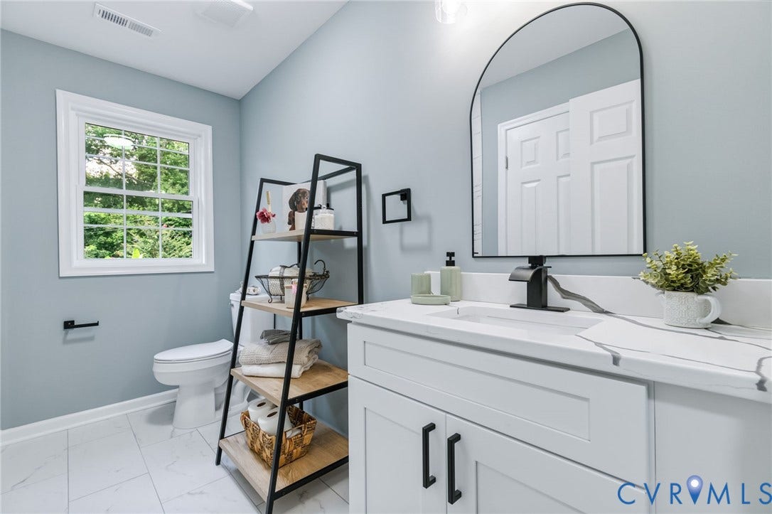 White single vanity with integrated sink and matte black faucet, arched mirror, white cabinetry with black hardware, and patterned floor tile