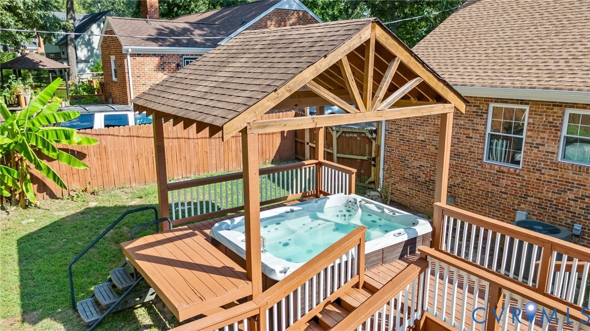 Outdoor spa with a wood-framed pergola, accessible from a multi-level wooden deck featuring stairs and railings