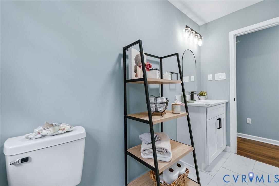 White vanity with black cabinet hardware, wall-mounted light fixture, and white floor tiling