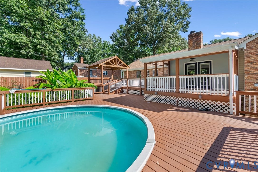 Large outdoor pool with a surrounding wood-finish deck, covered patio, and a separate covered gazebo structure