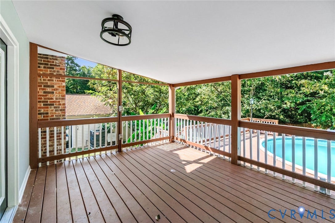 Covered outdoor deck with wood-finish flooring, white railing, and a black ceiling-mounted light fixture