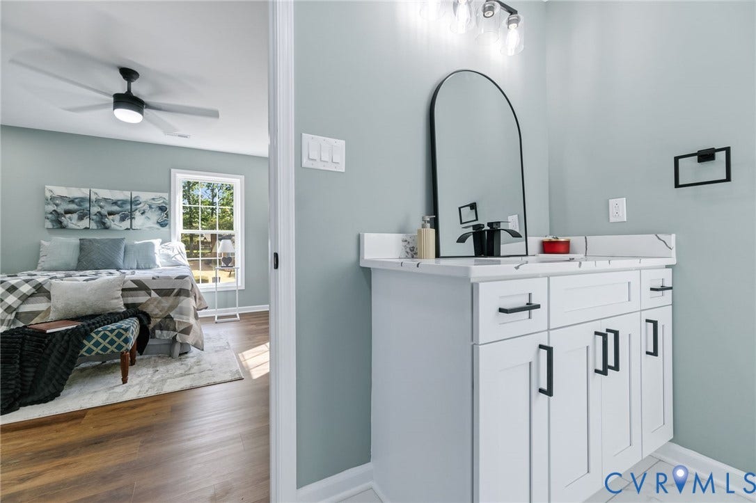 White vanity with black hardware, arched mirror, and multi-bulb light fixture