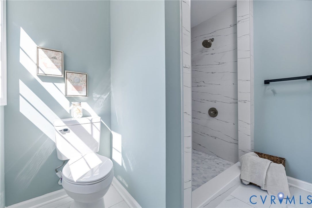 Walk-in shower with marble-look wall tiling and a tiled floor, accompanied by a white toilet
