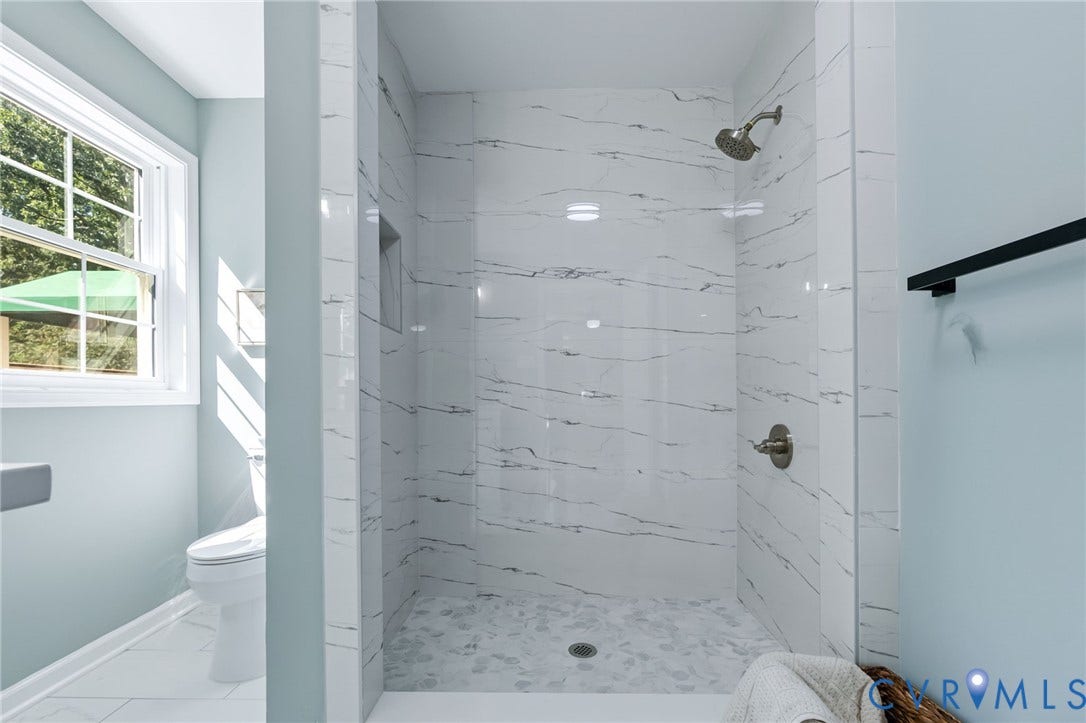Spacious shower with large format white tile walls featuring dark veining, a mosaic tile floor, and a recessed niche