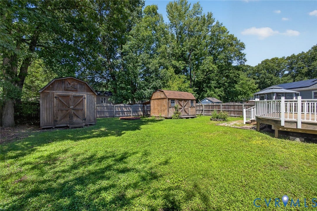 6302 Phobus Court, Richmond, VA 23234 Expansive backyard featuring a large wooden deck with white railings, two storage sheds, and a wooden privacy fence