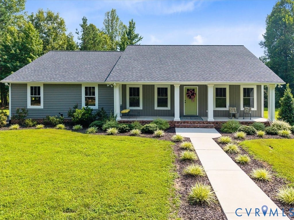 Ranch-style residence featuring horizontal siding, a covered porch with white columns, a gray shingle roof, a concrete walkway, and landscaped front beds