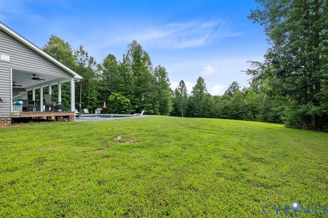 Expansive rear lawn framed by mature trees, featuring a covered porch with ceiling fans and an in-ground swimming pool