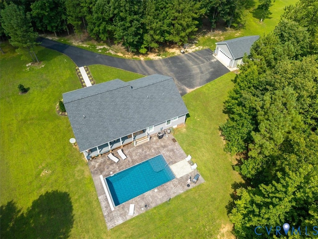 Expansive property featuring a rectangular swimming pool with surrounding concrete patio, a covered porch, and a detached two-car garage with an asphalt driveway