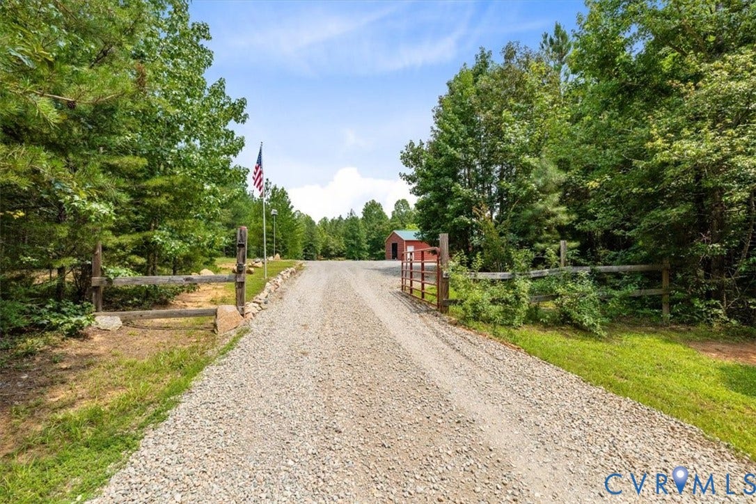 Gravel driveway framed by mature trees and natural wood fencing