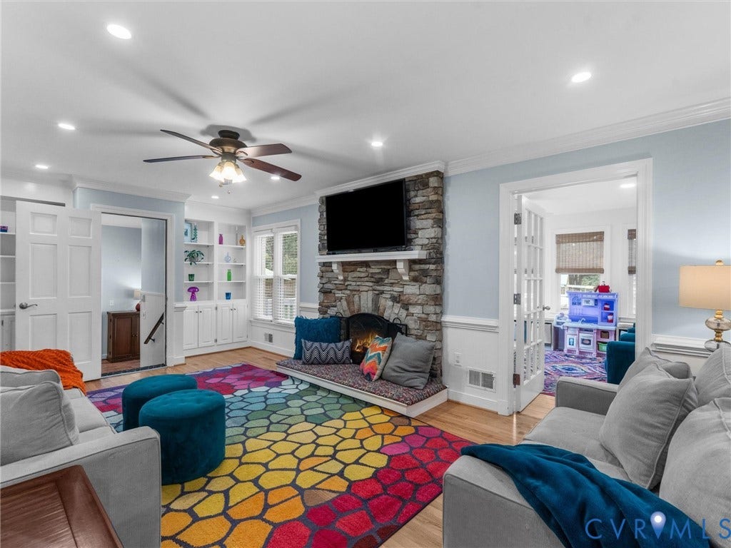 8216 Indian Springs Road, Richmond, VA 23237 Spacious recreation room featuring recessed lighting and ceiling fan, stone fireplace with mounted flat-screen television, hardwood flooring, built-in cabinetry with shelving, colorful geometric area rug, and multiple doorways providing access to adjacent spaces