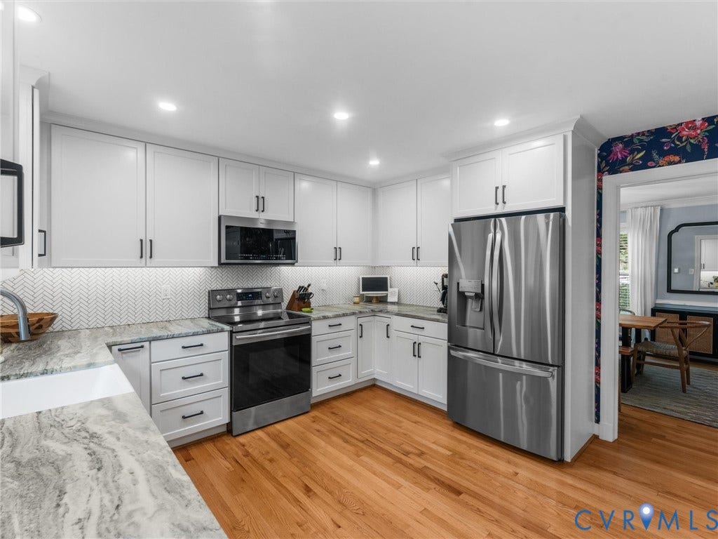 8216 Indian Springs Road, Richmond, VA 23237 L-shaped kitchen featuring white cabinetry with dark hardware, stainless steel appliances, patterned backsplash, light wood-finish flooring, and light-toned countertops