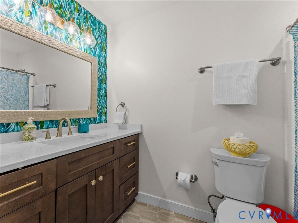 8216 Indian Springs Road, Richmond, VA 23237 Bathroom featuring a wood-finish vanity with a white countertop and integrated sink, gold-toned hardware, and a framed mirror with overhead lighting