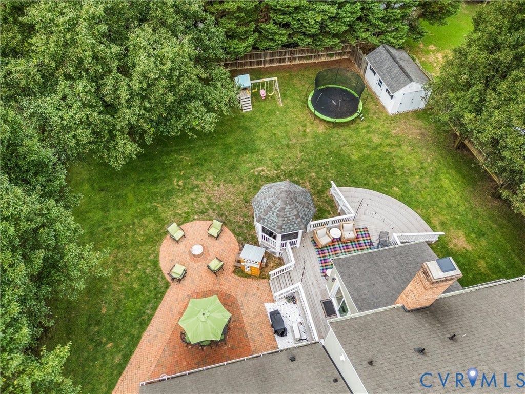 8216 Indian Springs Road, Richmond, VA 23237 Expansive backyard oasis featuring a circular brick patio with seating areas, in-ground trampoline, mature tree canopy, detached shed structure, and manicured lawn bordered by natural woodland
