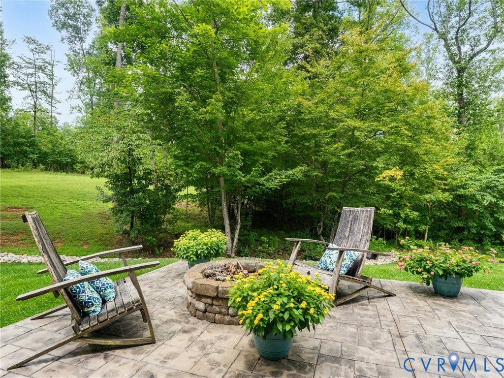 3647 Walkers Creek, Powhatan, VA 23139 Expansive backyard oasis featuring a stone-paved patio, circular fire pit with brick surround, mature landscaping with lush green lawn, and abundant tree canopy providing natural shade and privacy