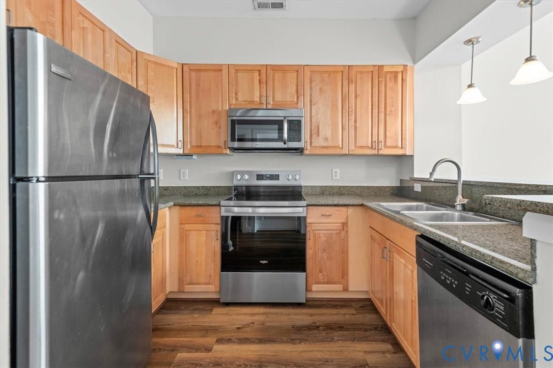 1333 Broad Street, #510, Ironhouse Place Condominiums, Richmond, VA 23220 Kitchen featuring wood-finish flooring, light wood cabinetry, stainless steel appliances, and dark speckled countertops