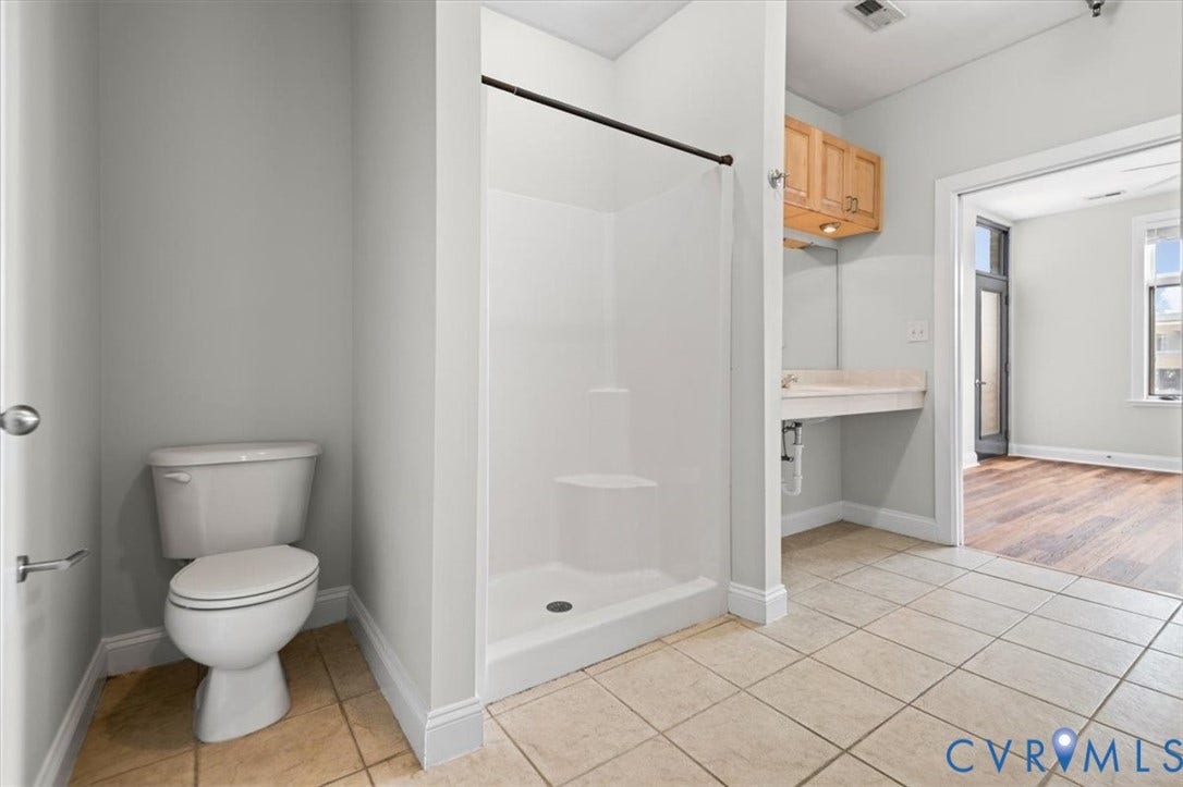 1333 Broad Street, #510, Ironhouse Place Condominiums, Richmond, VA 23220 Three-quarter bathroom featuring a white toilet, enclosed shower stall with a black curtain rod, and light-toned tile flooring