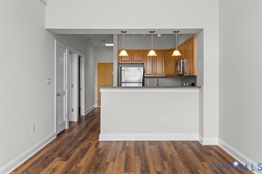 1333 Broad Street, #510, Ironhouse Place Condominiums, Richmond, VA 23220 Kitchenette with wood-finish flooring, light wood cabinetry, stainless steel appliances, and a breakfast bar with three pendant lights