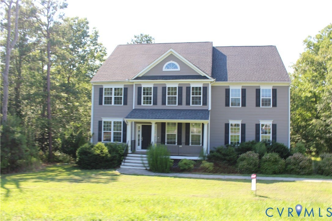 Two-story residence featuring grey siding with dark shutters, a front porch with white columns, and an arched transom window above the main entry