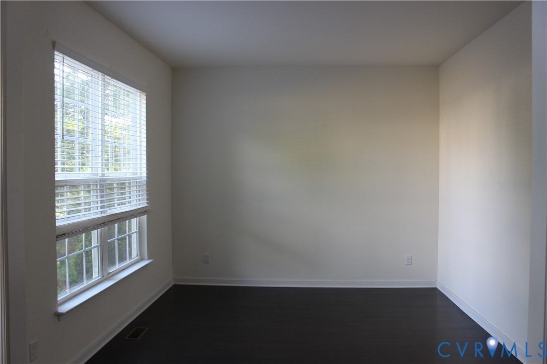 Spacious room featuring a large window with white blinds, dark wood-finish flooring, and light-colored walls