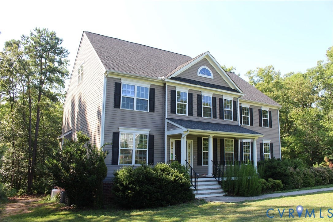 Two-story residence featuring light gray siding, dark shutters, and a covered front porch with white columns