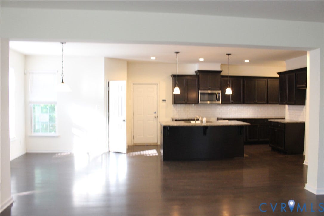 Kitchen with dark wood-finish cabinetry, a large center island with pendant lighting, and stainless steel appliances