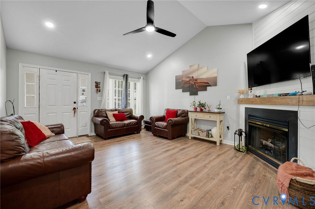 5612 Jessup Station Place, Chesterfield, VA 23234 Living room featuring wood-finish flooring, a vaulted ceiling with recessed lighting and a ceiling fan, a fireplace with a white shiplap surround and a wood mantle, and a white double entry door with clear glass side panels