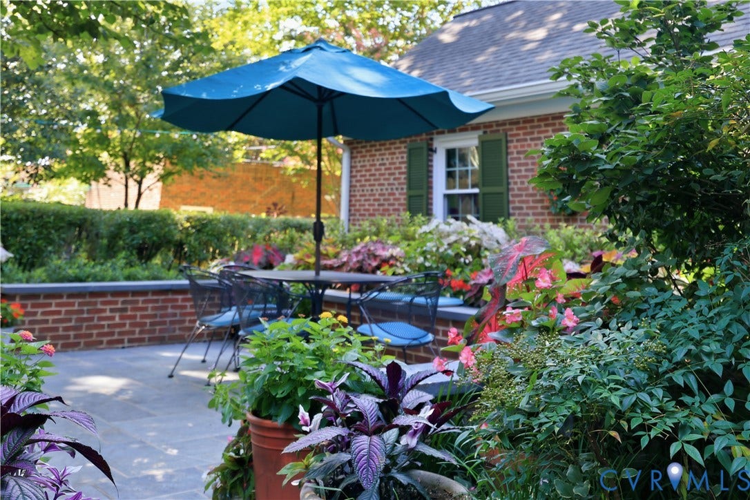 4207 W Grace Street, Sauer's Gardens, Richmond, VA 23230 Outdoor patio featuring slate-style paving, a low brick retaining wall, and verdant landscaping