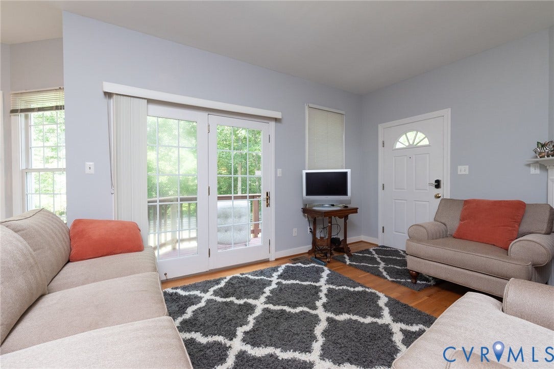 4280 Hadensville Farm Road, Hadensville Farms, Mineral, VA 23117 Living area featuring hardwood flooring, a white paneled entry door with an arched transom, a fireplace with a white mantel, and a dark stone surround