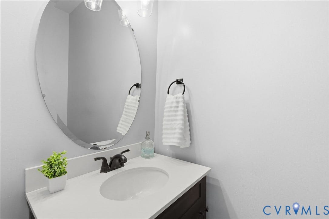 8343 Shagreen Court, The Highlands, Chesterfield, VA 23838 Oval mirror with a beveled edge, vanity light fixture, white countertop, dark wood-finish vanity, and bronze-finish faucet