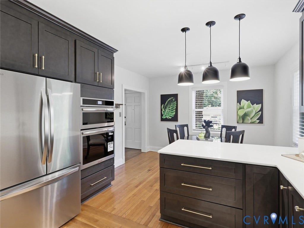 Stainless steel appliances, built-in double ovens, dark wood-finish cabinetry, white countertops, and warm wood-finish flooring