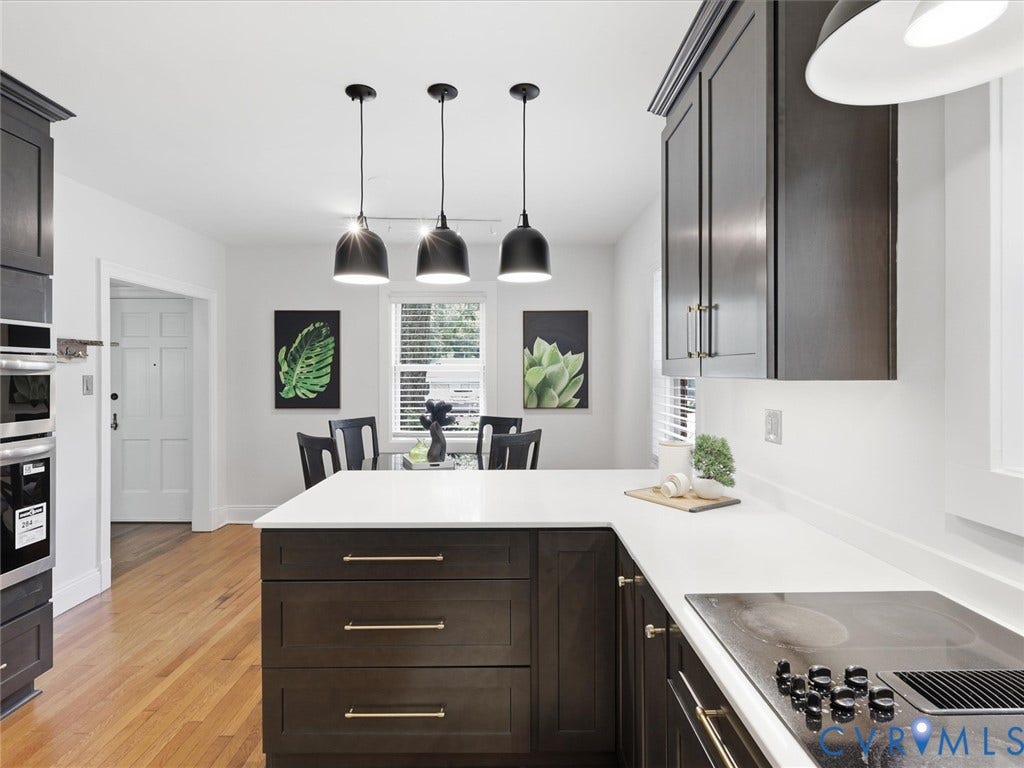 Dark wood-finish cabinetry with gold-tone hardware, white countertops, built-in double ovens, and a built-in cooktop