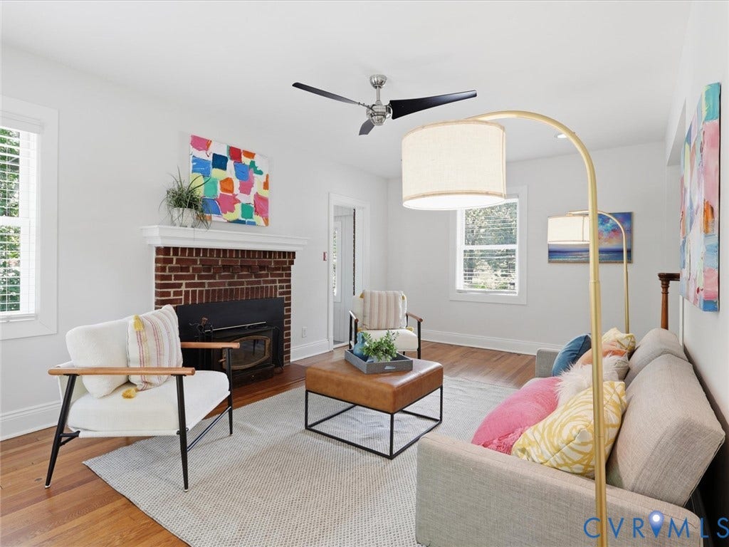 Bright living room featuring hardwood flooring, a brick fireplace with dark surround, and large windows providing natural light