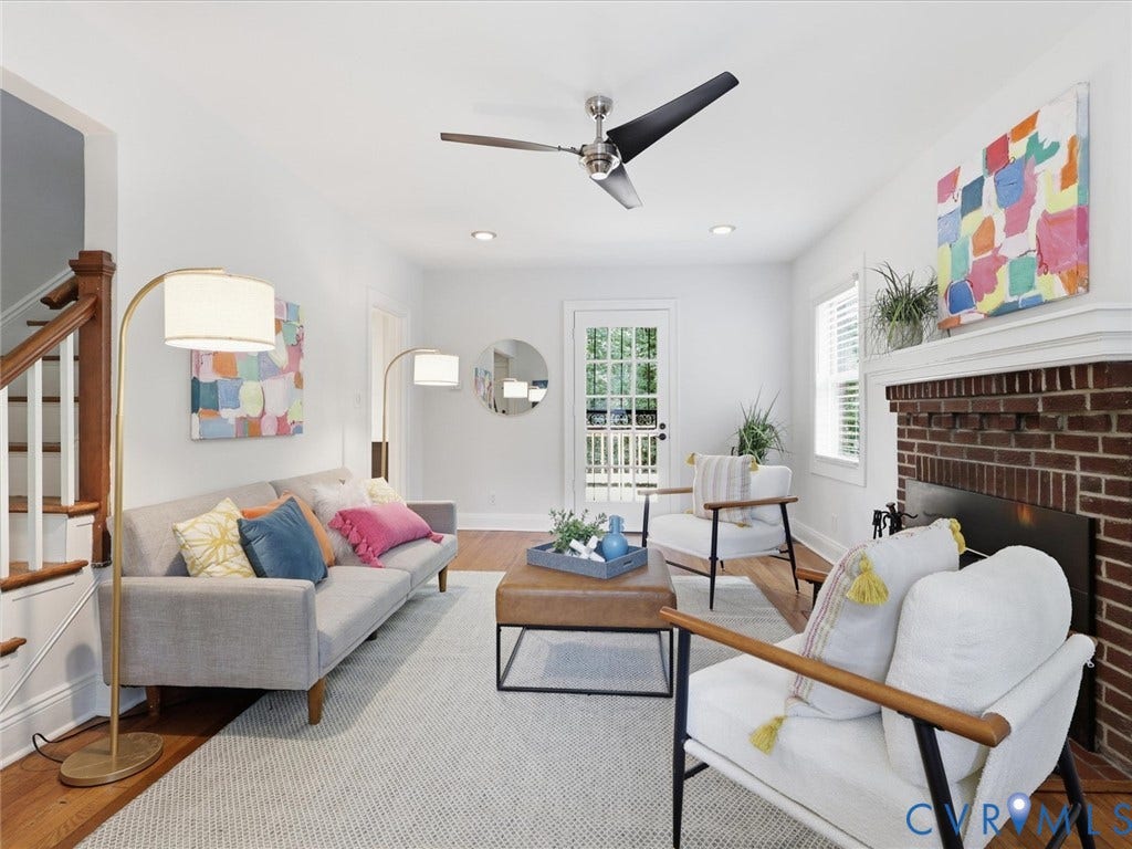 Hardwood flooring, brick fireplace with mantel, ceiling fan, white paneled walls, and staircase with wood banister