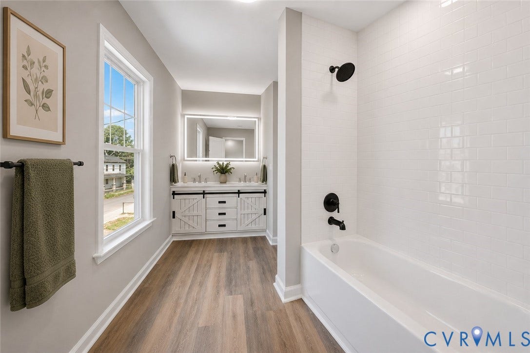 425 BYRNE Street, Petersburg, VA 23803 Dual sink vanity with barn door style cabinetry, large back-lit mirror, white subway tile bath surround, dark bronze fixtures, and wood-finish flooring