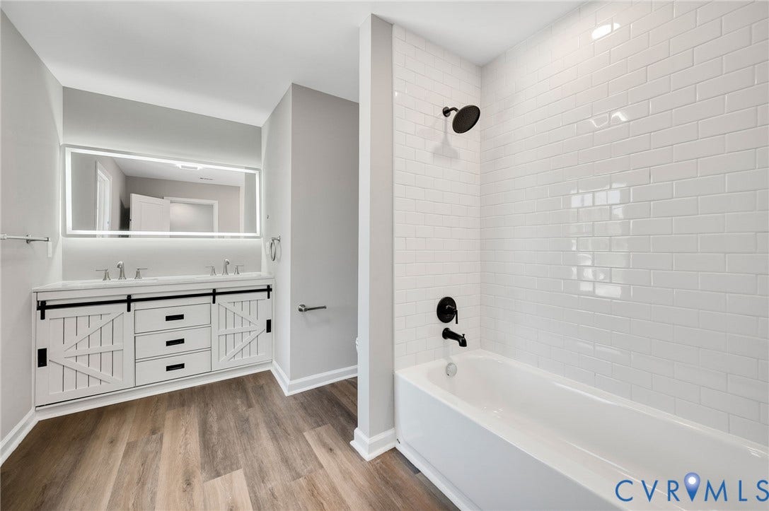 425 BYRNE Street, Petersburg, VA 23803 Modern bathroom featuring a double vanity with barn-door style cabinetry, an illuminated mirror, and wood-finish flooring