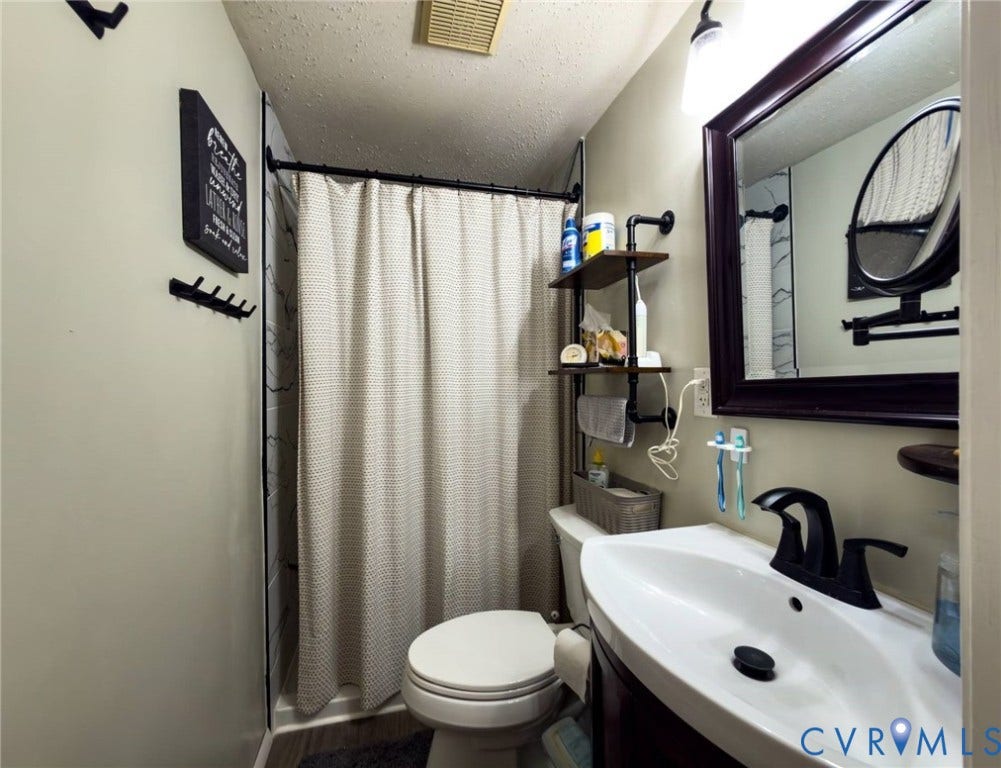 4900 Cord Court, Bridgewood, Glen Allen, VA 23060 Modern bathroom featuring a white ceramic vessel sink with matte black faucet, framed mirror with dark trim, white subway tile shower surround with coordinating curtain rod, and open shelving with integrated storage