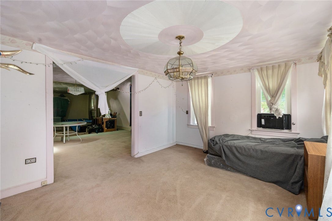5927 Swanson Road, Richmond, VA 23225 Carpeted room featuring a ceiling medallion, central chandelier lighting, two windows with drapes, and an entryway to an adjacent space