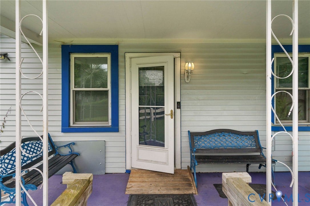 5927 Swanson Road, Richmond, VA 23225 Front porch entrance featuring a white storm door with glass panels, a sconce light fixture, and two single-hung windows with blue trim