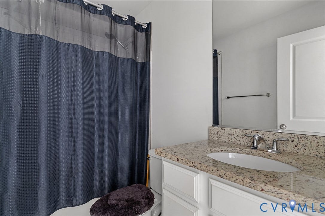 Spa-inspired bathroom featuring dual vanities with speckled stone countertops, a framed mirror with integrated lighting, and a coordinating tile shower enclosure with glass panel and chrome fixtures